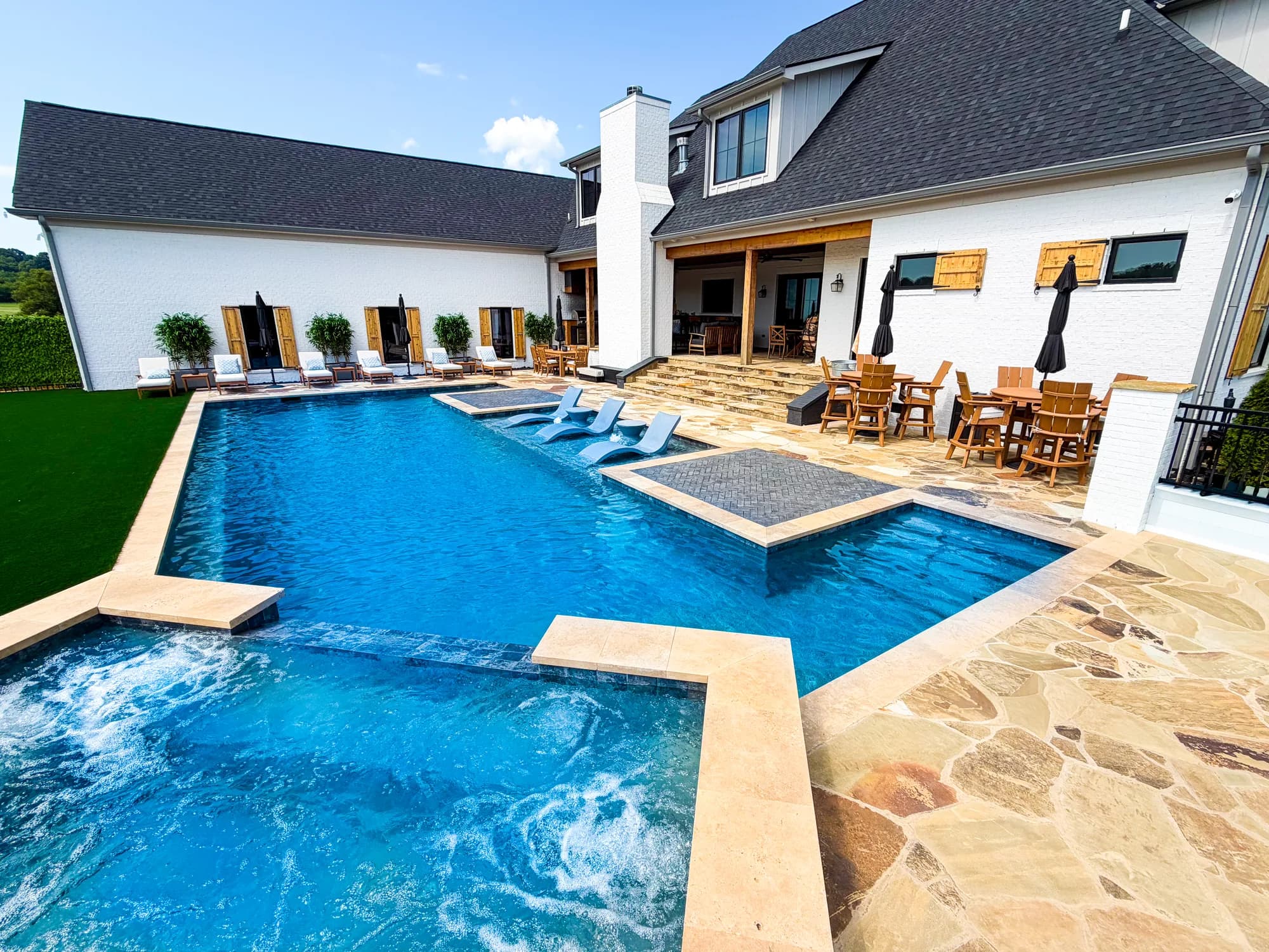 Bright blue custom pool with travertine deck and loungers behind a white home in Murfreesboro, TN